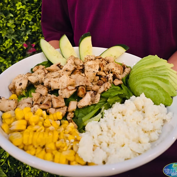 A vibrant Vallarta Mexican Grill salad with chicken, corn, avocado, cheese, and cucumber slices.